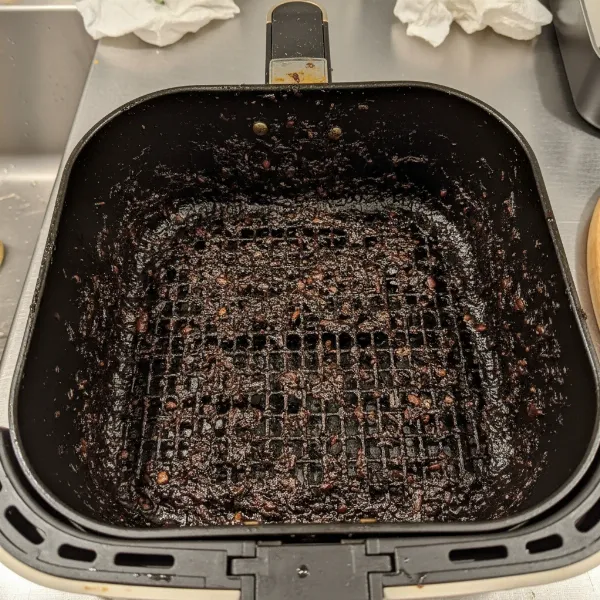 Heavily greased air fryer basket with stubborn baked-on food residue and oil buildup.
