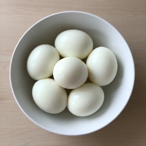 A white bowl filled with several smooth, perfectly peeled hard-boiled eggs on a clean surface.